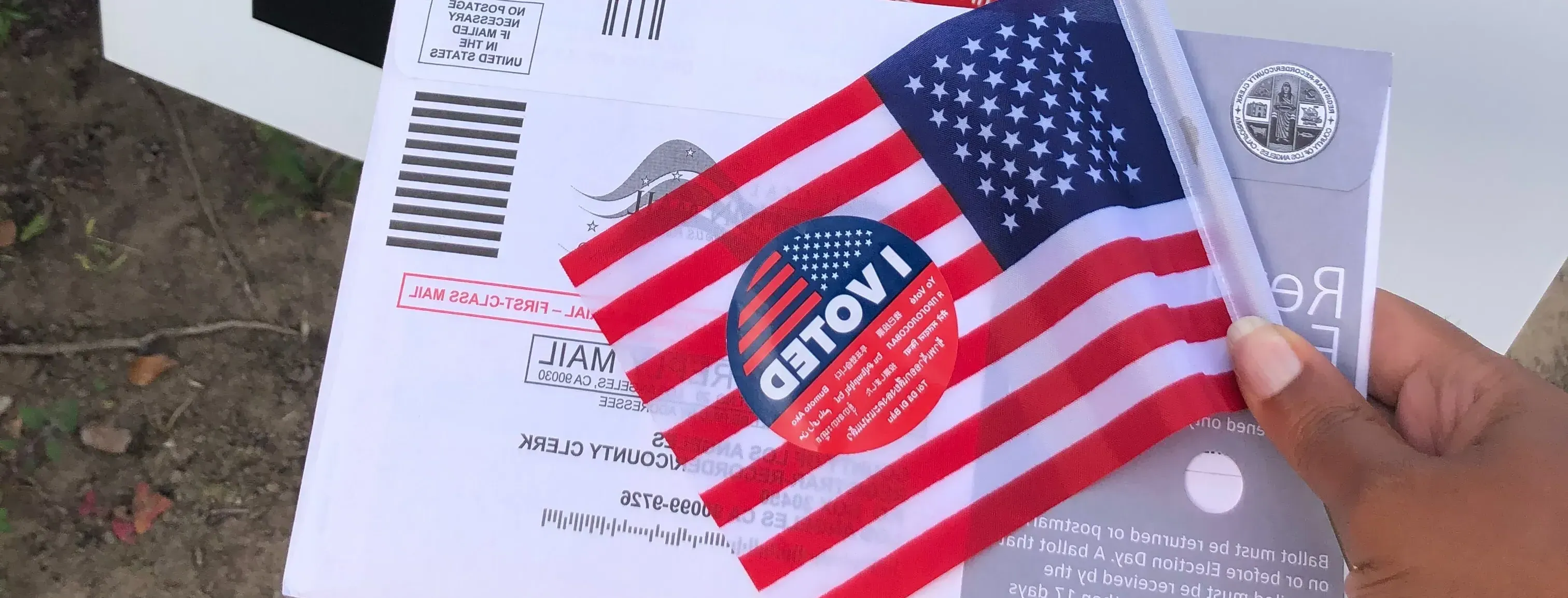 A person holds up an "I Voted" sticker, along with their ballot.